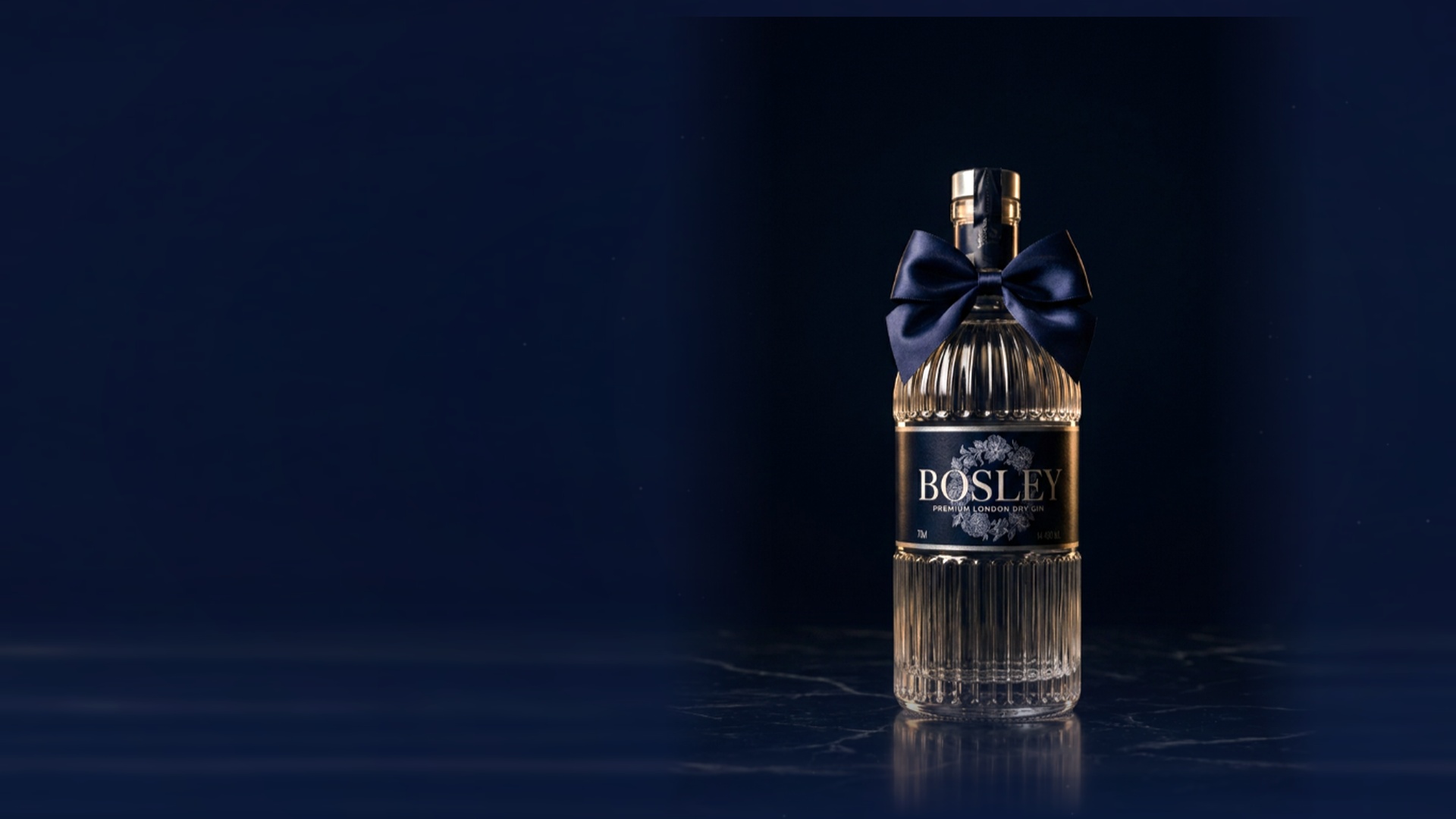 A bottle of Bosley Premium London Dry Gin, ribbed glass with its deep navy satin bow and navy floral-wreath label, standing on polished black marble in low light